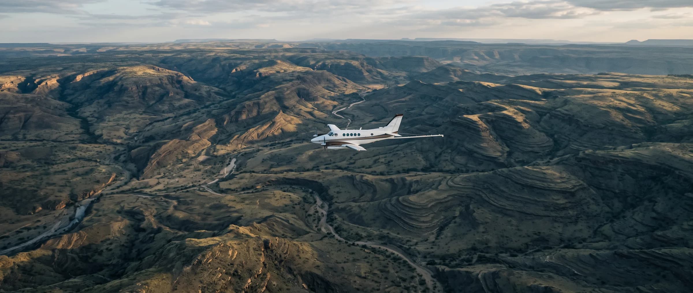 A geophysical survey aircraft flying low over highland terrain whose ridges read as geological contour lines.
